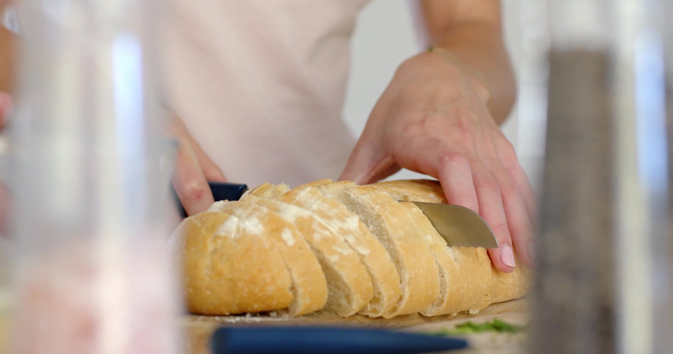 Donna che posiziona una pagnotta su un tagliere, la tiene ferma e taglia il pane con un coltello, preparando un pasto.