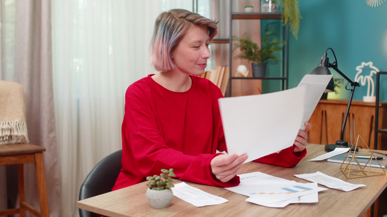 Young woman happily reviewing financial documents nodding positively satisfied successful results