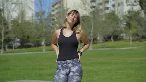 Smiling-sporty-young-woman-standing-on-green-meadow