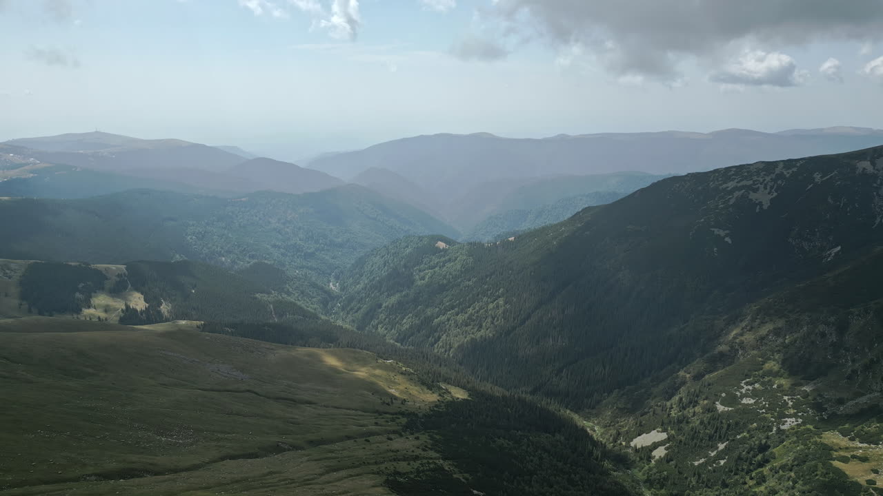 Affascinante veduta aerea della serena regione Transalpina in Romania, che mette in risalto vaste valli boscose, catene montuose ombreggiate e prati aperti incontaminati sotto un cielo dolcemente nuvoloso