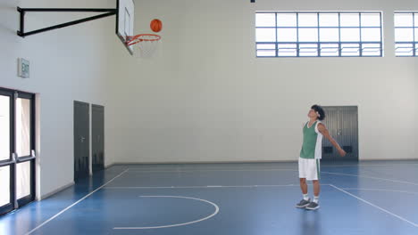 young biracial man plays basketball indoors