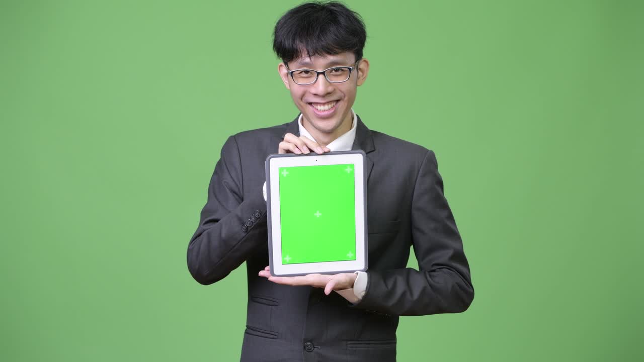 젊은 행복한 아시아 사업가들이 디지털 태블릿을 카메라에 보여주고 있습니다.