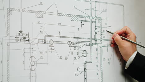 a hand points at a technical drawing or blueprint