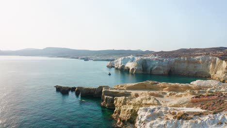 sarakiniko beach coastline with a boat sailing the mediterranean sea in milos greek island, drone shot dolly in