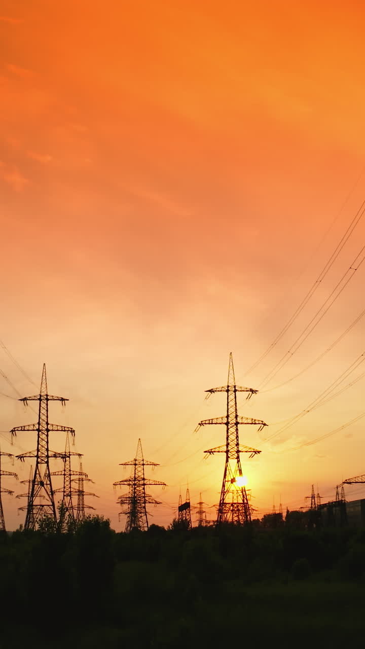 Transmission lines under red evening sky. High-voltage electric towers with wires in nature at beautiful sunset. Power lines against the backdrop of setting sun. Vertical video