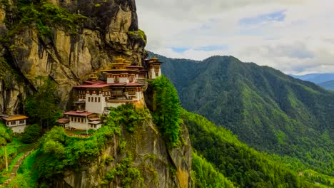 timelapse footage of the taktsang palphug monastery and the tiger's nest on a sharp steep cliff edge during a sunny day while cloud shadows are going over the temple architecture and green nature.