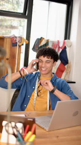 vertical video of biracial male fashion designer talking on smartphone in studio, slow motion