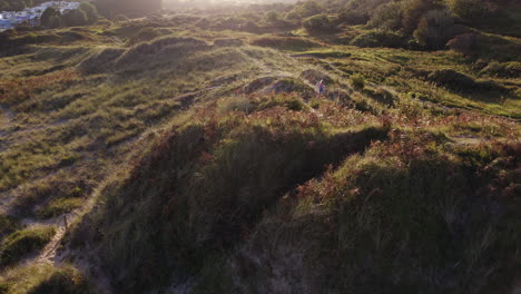 Drohnenaufnahme-Eines-Jungen-Mädchens-Im-Strandurlaub,-Das-In-Sanddünen-Vor-Der-Flackernden-Sonne-Spielt