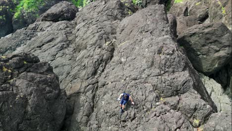 Traveler-climbing-down-a-jagged-volcanic-rock-boulder-in-Catanduanes,-Philippines