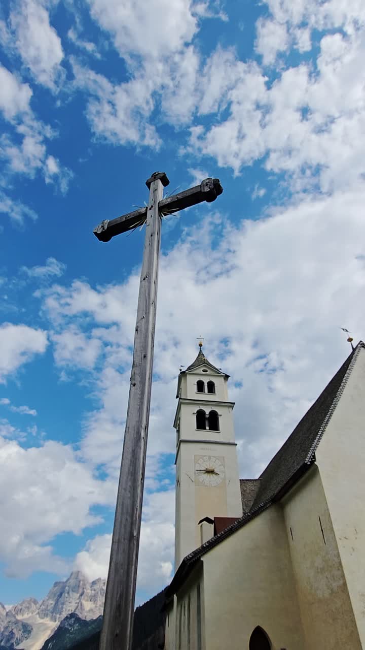 Rustic wooden cross with historical bell tower against blue sky in Villagrande