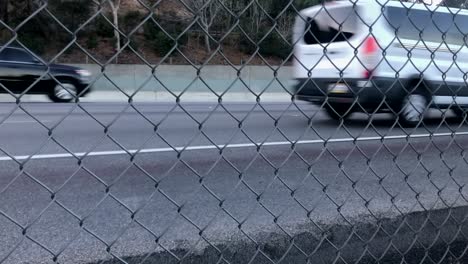 vehículos que circulan por una autopista concurrida, vista abstracta a través de la cerca de eslabones de cadena