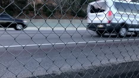 vehicles driving on busy freeway, abstract view through chainlink fence