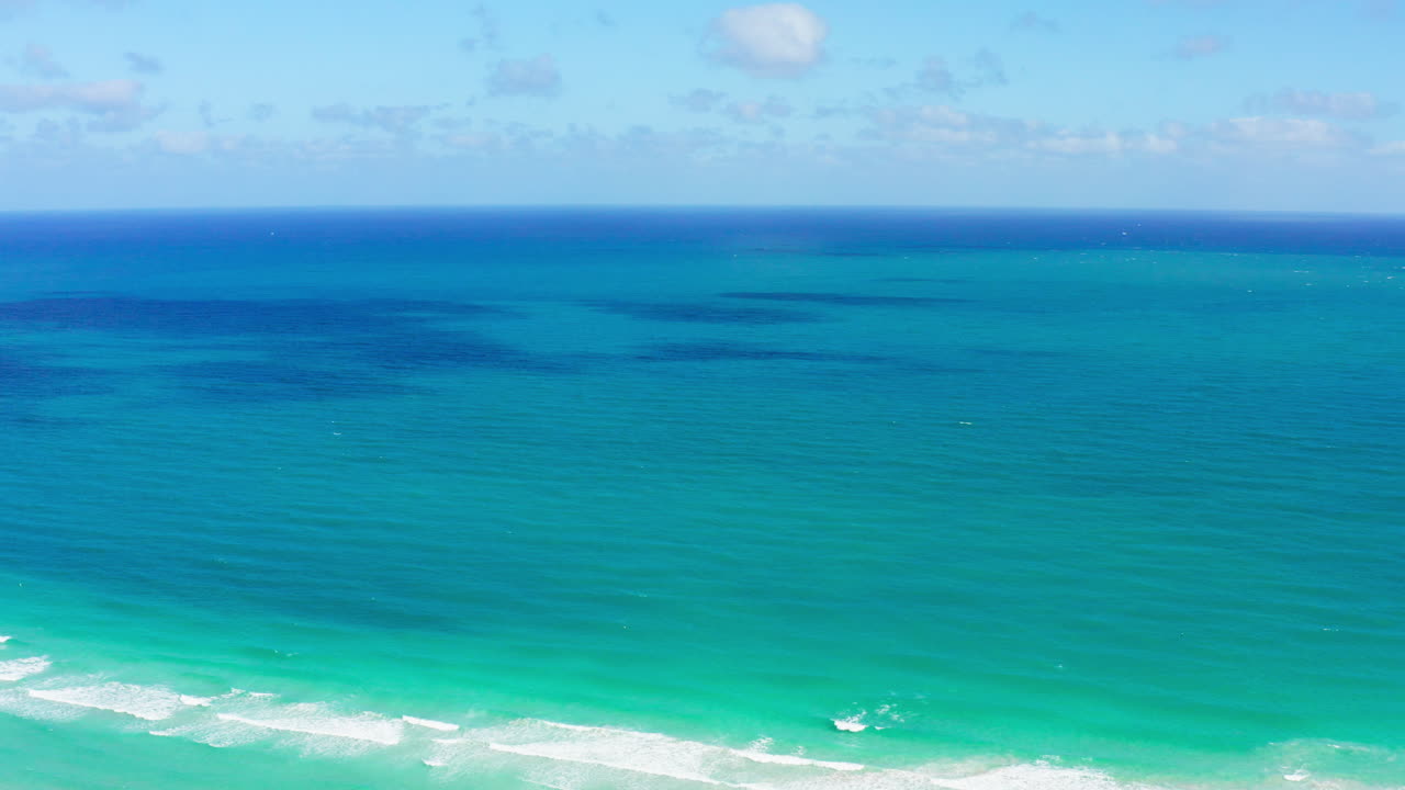 A serene drone fly-in captures the vast turquoise waters of the Atlantic Ocean gently meeting South Beach’s white shore under a bright, clear sky.