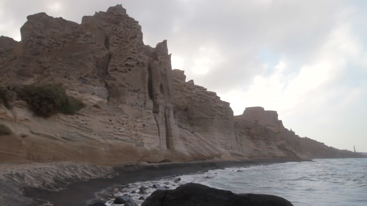 Static shot of a black beach surrounded by white volcanic cliff formations getting hit by waves