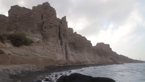 Static-shot-of-a-black-beach-surrounded-by-white-volcanic-cliff-formations-getting-hit-by-waves