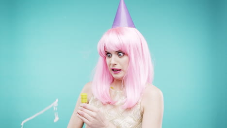 woman with pink hair in party hat, surprised by balloons