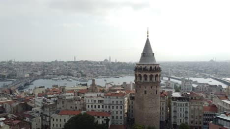 Vista-Aérea-De-Paralaje-De-La-Torre-De-Gálata-En-Beyoglu-Estambul-Con-El-Mar-Del-Bósforo,-Las-Mezquitas,-El-Puente-De-Gálata-Y-La-Silueta-De-La-Ciudad-De-Estambul-En-El-Fondo-Detrás