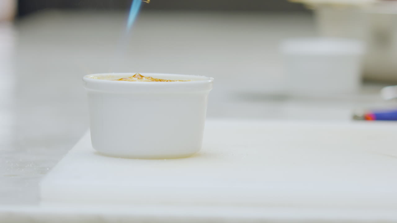 Close-up of a creamy dessert creme brulee served in a ceramic mold is torched to give it a golden color on a white counter