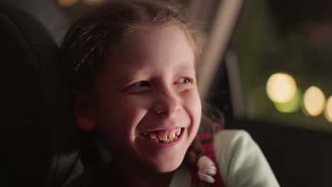 a close view of a child in a car smiling with blurred lights seen through the car window, capturing a joyful moment during a nighttime drive