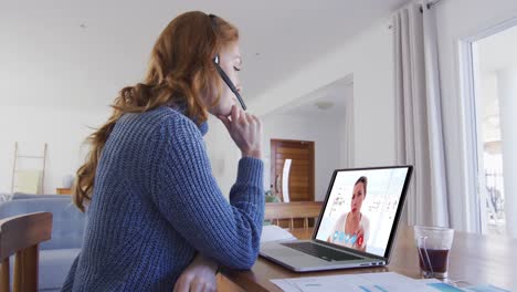 mujer caucásica usando portátil y auriculares de teléfono en videollamada con una colega