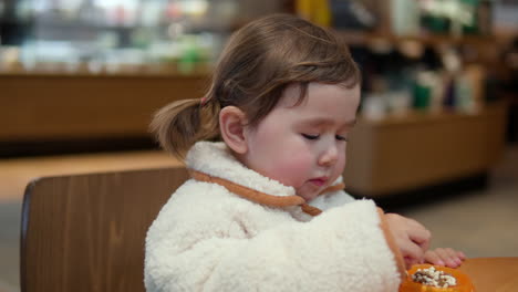 cute caucasian child girl eating tasty chocolate balls snacks sitted by the table - portrait