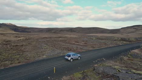 a car drives through iceland's barren landscape, surrounded by volcanic rock and moss