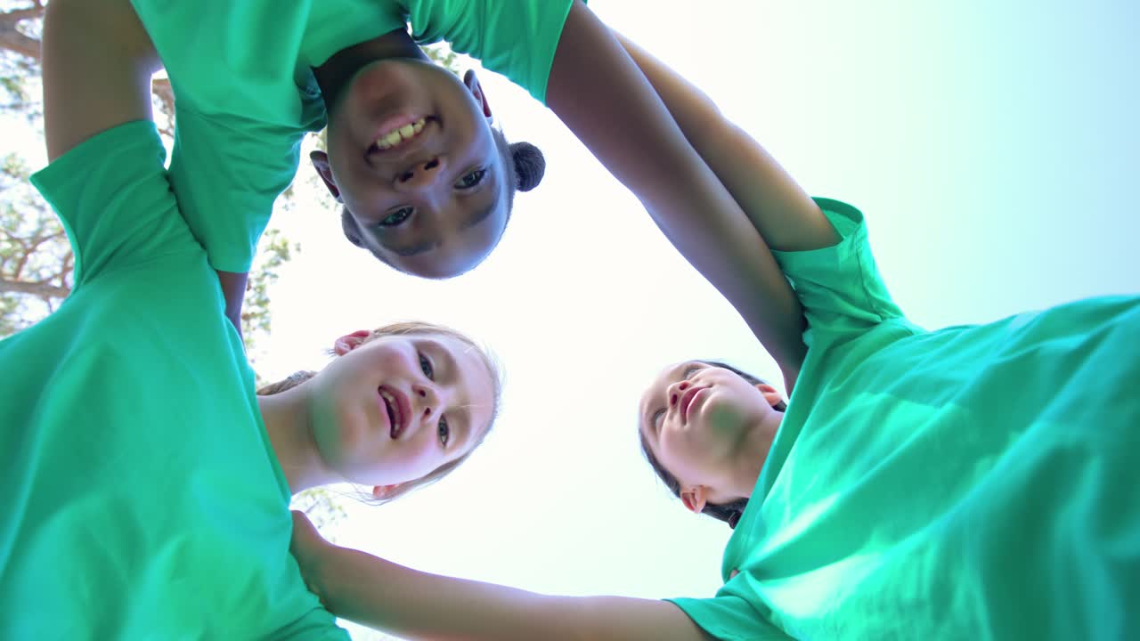 Three youth females forming huddle after cue linking leaning reaching low camera lens in green tees