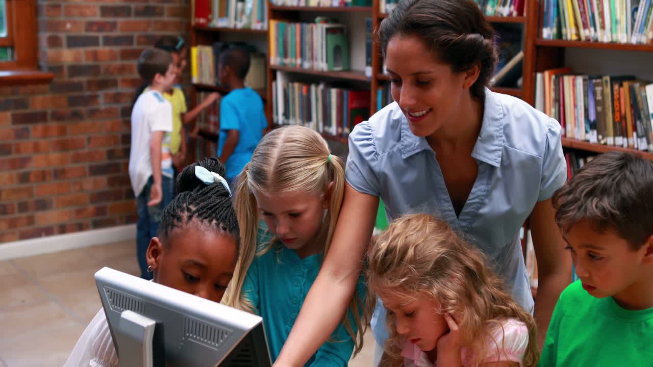 alumnos mirando la computadora en la biblioteca con su maestro