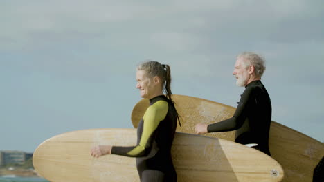 medium shot of a senior couple in wetsuit holding surfboard and running into the ocean