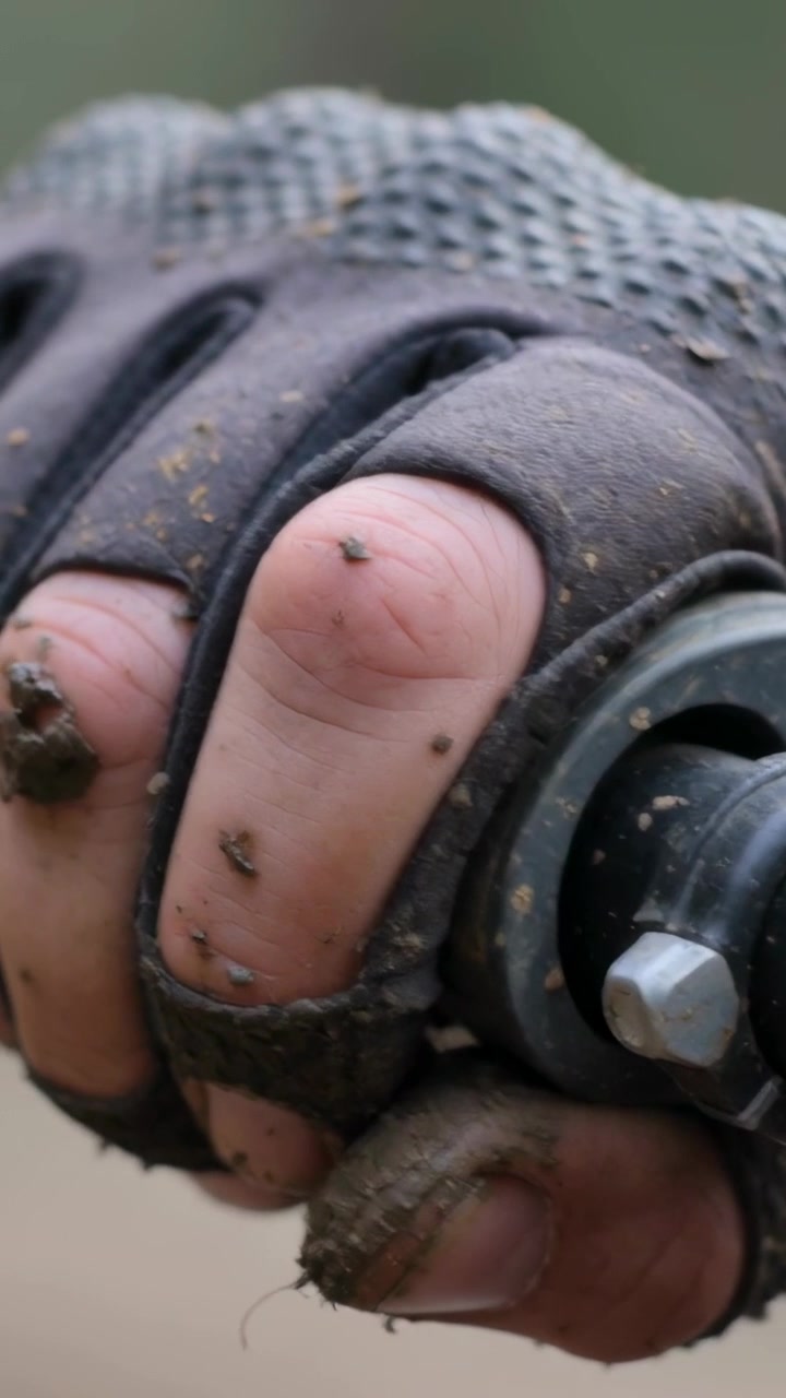 Video verticale: Mano con guanto senza dita infangato che afferra e gira un dado metallico su un'asta all'aperto per fissare.