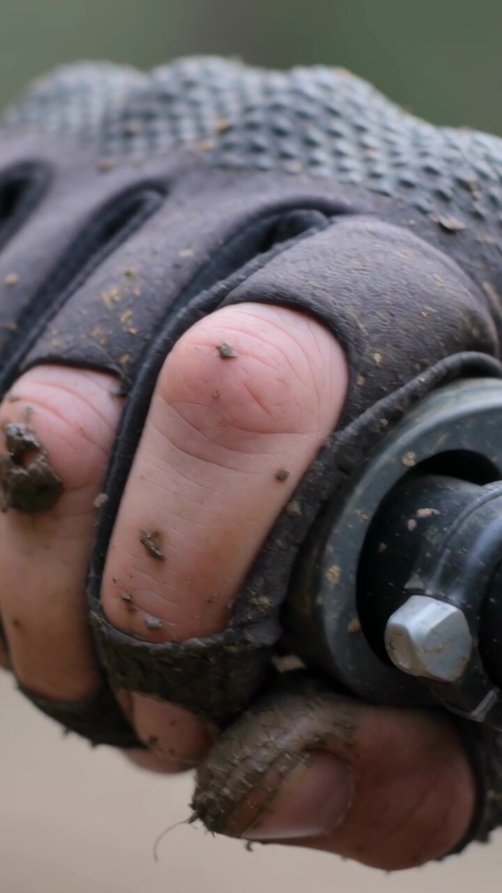 Vertical video: Gripping muddy fingerless glove hand turning metal nut on rod outdoors to secure