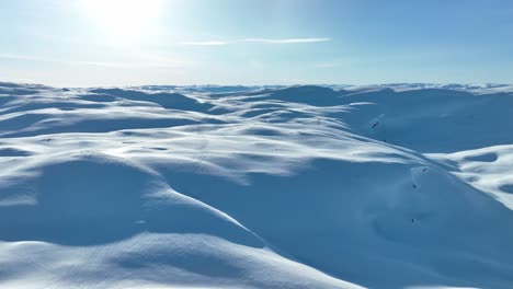 Ski-tracks-and-high-voltage-powerlines-disappearing-into-vast-snowy-mountain-landscape-during-sunset---Vikafjell-western-Norway-winter-aerial