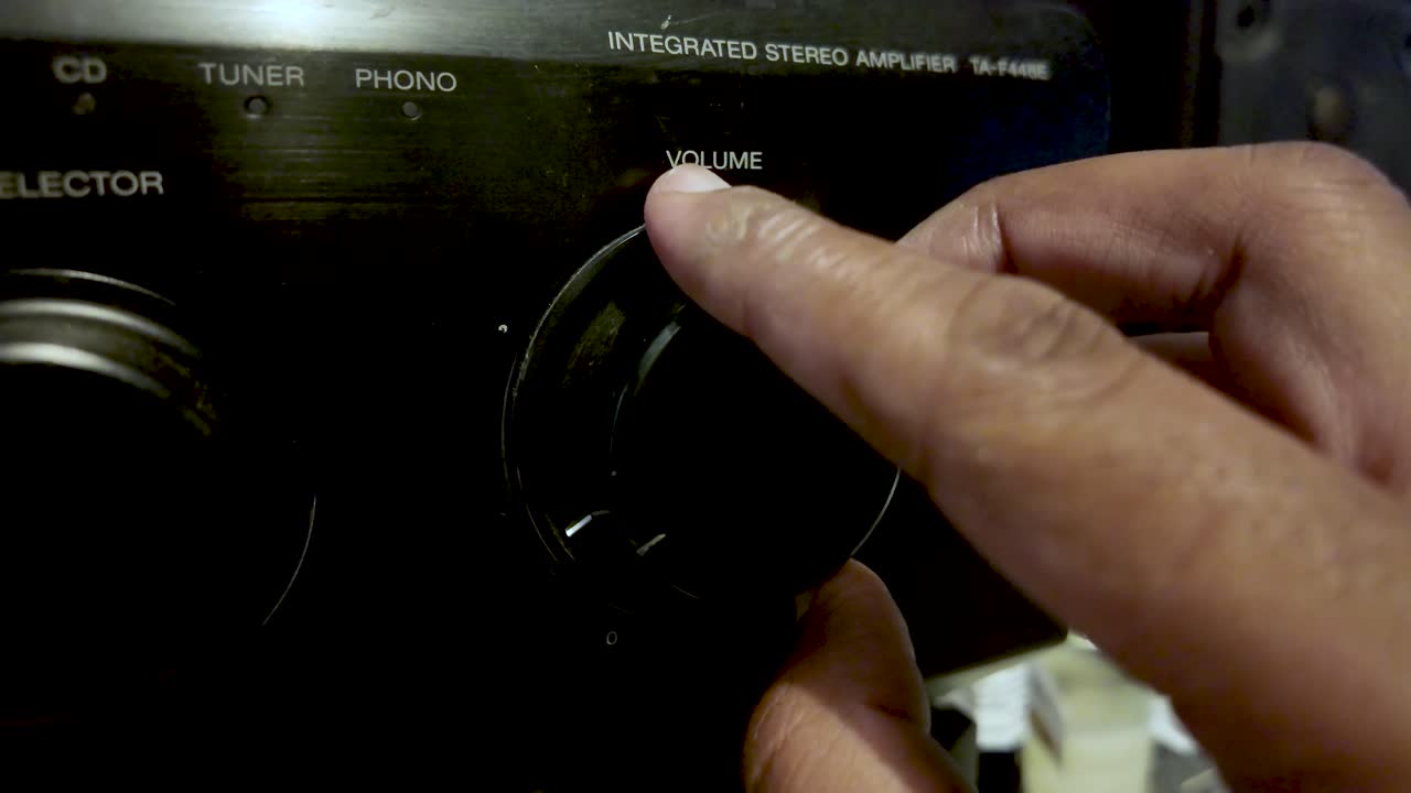 Close-up of hands turning a volume knob on a classic integrated stereo amplifier, capturing tactile control and vintage vibe