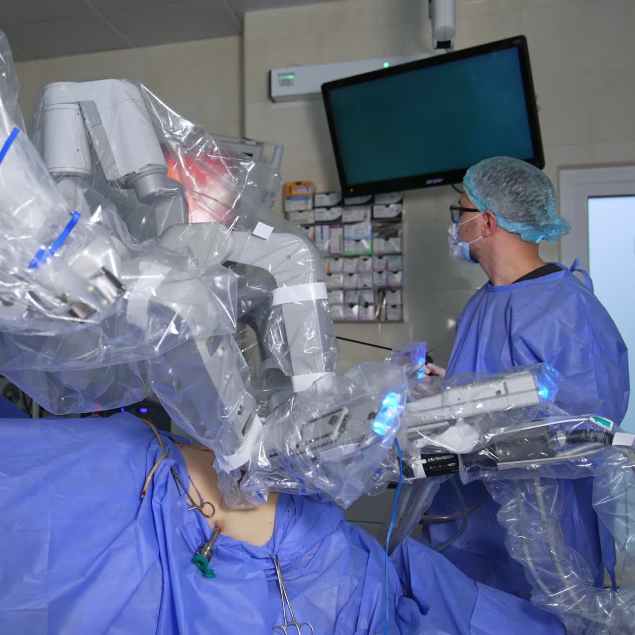 Technological robotic equipment conducting laparoscopic surgery I modern operational theatre. Male medic takes the instrument and looks at the screen