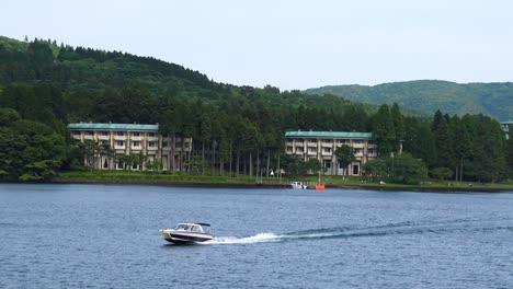 the view of ashi lake and some buildings, with a motorboat passing by