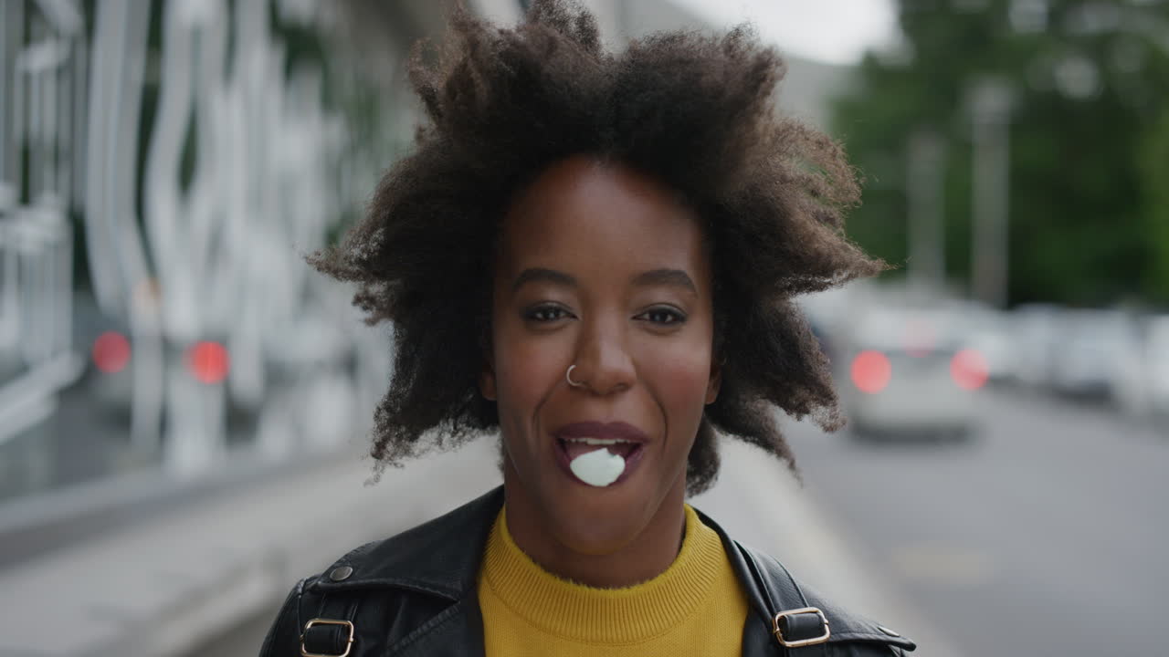 retrato de una joven afroamericana soplando chicle dulce disfrutando de diversión juguetona estudiante negra afro funky en la calle de la ciudad urbana