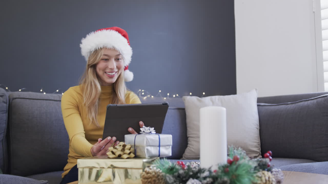 feliz mujer biracial con sombrero de papá noel usando tableta para video llamada de navidad, en cámara lenta