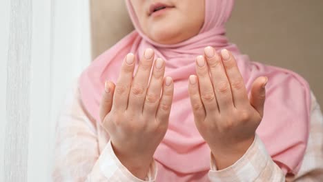 unrecognizable woman in pink hijab reads a prayer holding hands in front of her and washes face