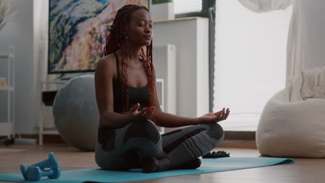 Flexible-black-athlete-relaxing-in-lotus-position-on-floor-in-living-room