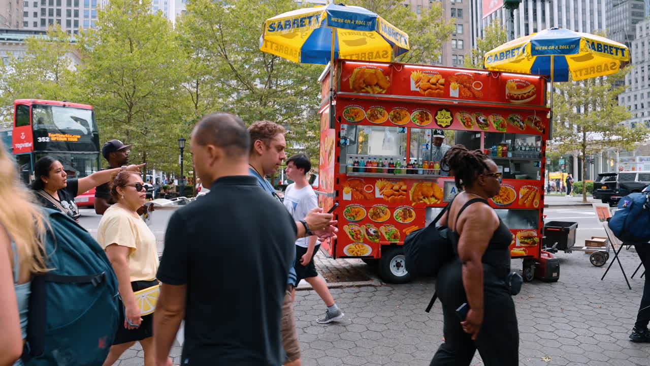 New York, USA, 8. juli 2025: Farverig madvogn på en gade i New York. Mange mennesker går langs fortovet