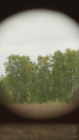 warrior looks through binoculars surveying birch grove. soldier waits for enemy in ambush using optical tracking device. spying from inconspicuous place