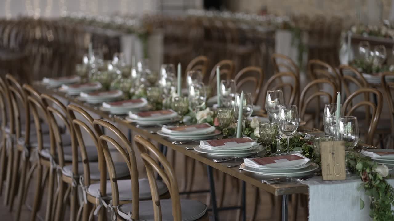 Lange, elegant dekkede bryllupsbord med blomsterdekorasjoner og trestoler i en festsal