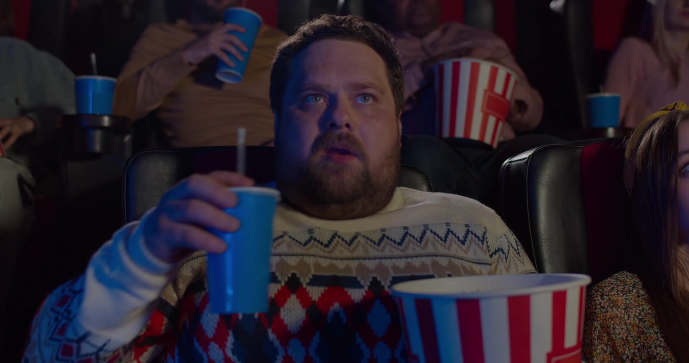 Mand spiser popcorn og drikker sodavand i biografen