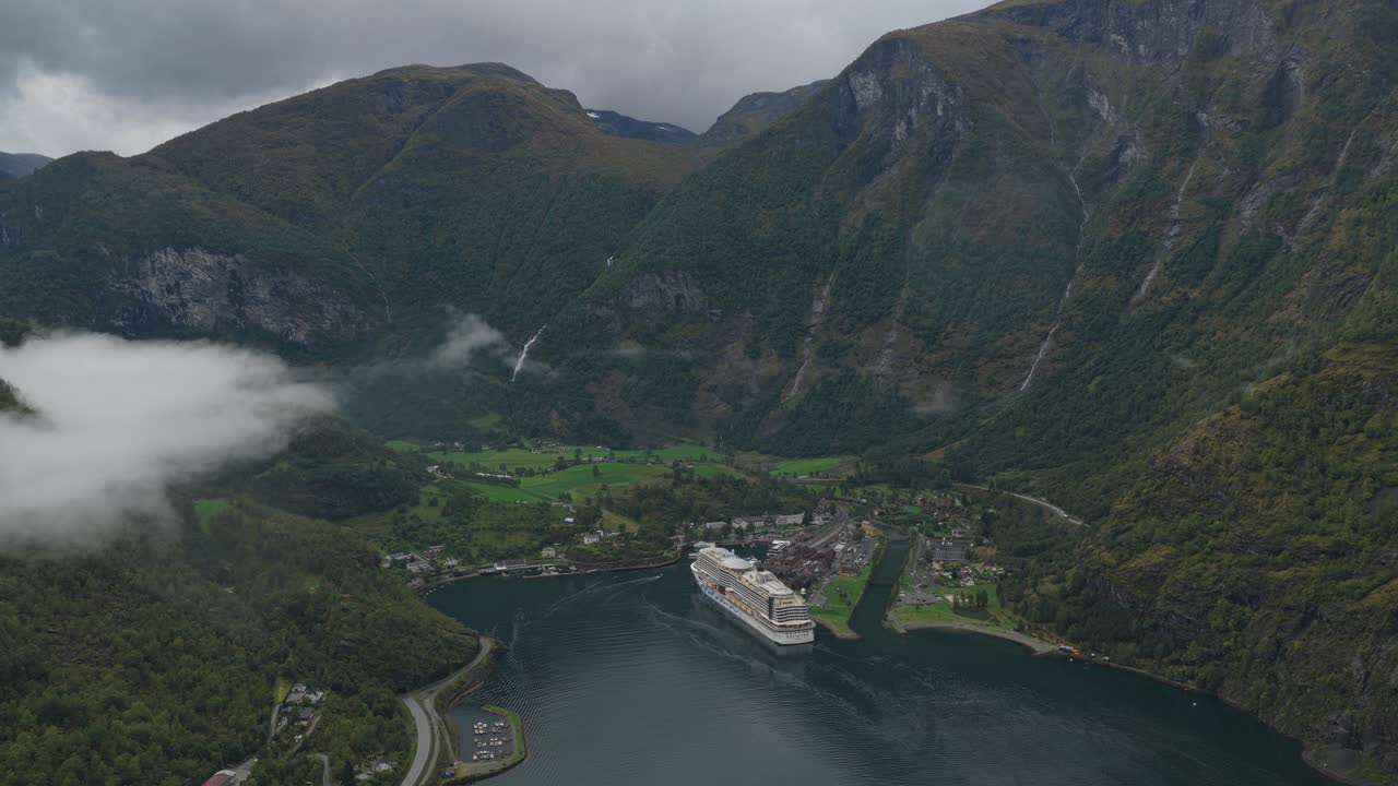 Drohnenaufnahme von oben des Hafens Flam und eines Kreuzfahrtschiffs, umgeben von dramatischer norwegischer Natur