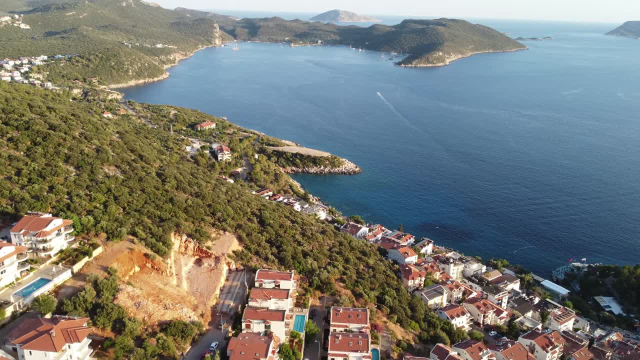 Aerial drone shot showing tranquil peninsula with island dotted horizon along coastal waters near Akyaka in Mugla, capturing green hills, seaside homes, calm blue sea, and warm late afternoon light