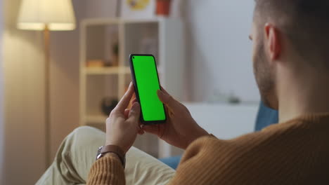 joven está navegando por internet y las redes sociales con un teléfono inteligente moderno desplazando la pantalla táctil chroma clave en la pantalla descansando en casa con gadgets adicción a internet