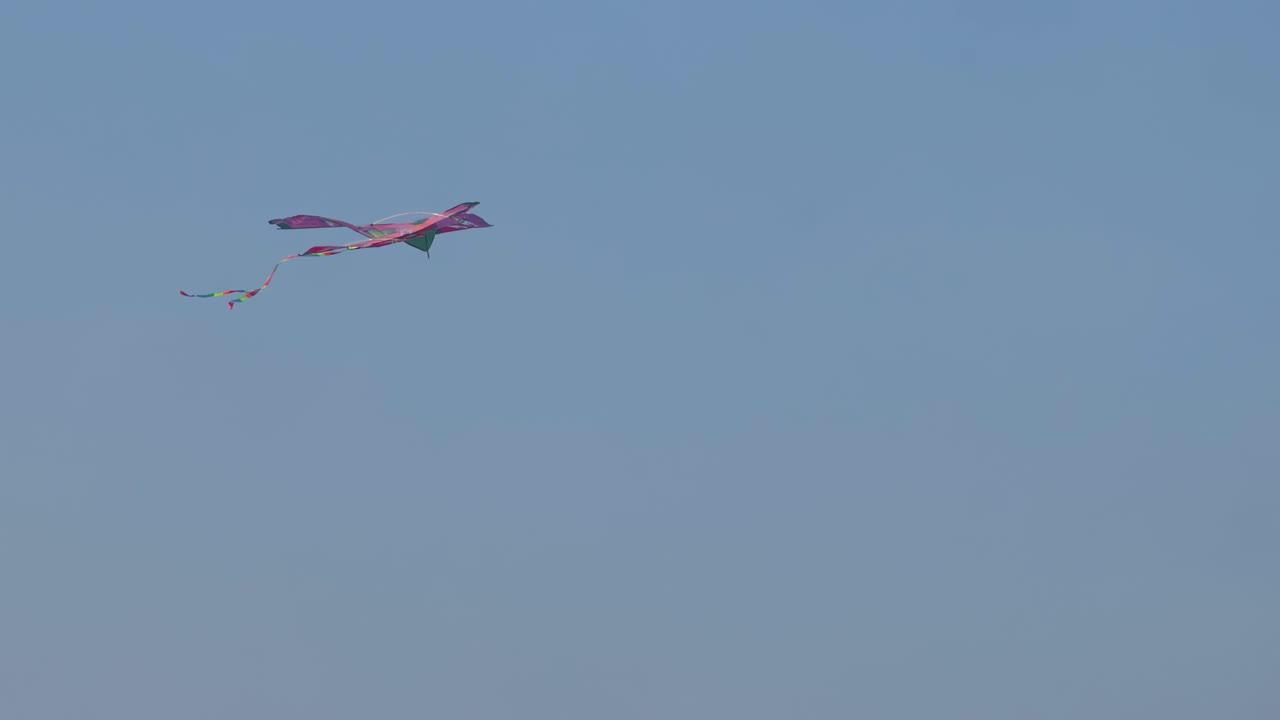 A vibrant red kite gracefully glides and twirls against a clear blue sky, showcasing its colorful tail.