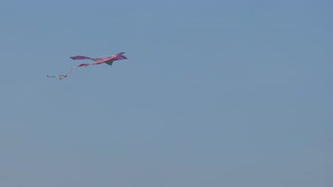 a vibrant red kite gracefully glides and twirls against a clear blue sky, showcasing its colorful tail.