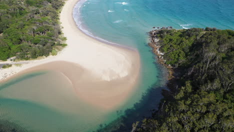 Wide-drone-shot-of-the-South-Pacific-Ocean-and-Korogoro-Creek-with-wind-blowing-sand-across-a-sand-bar-at-Hat-Head-New-South-Wales,-Australia