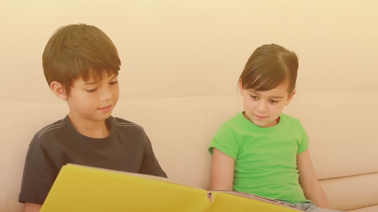 백인 형제가 집에서 여동생에게 책을 읽고 있습니다.